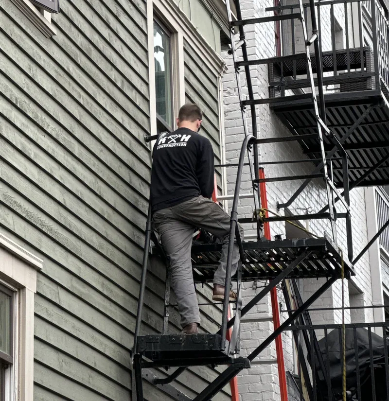 Fire escape technician climbing onto a steel landing during a hands-on inspection